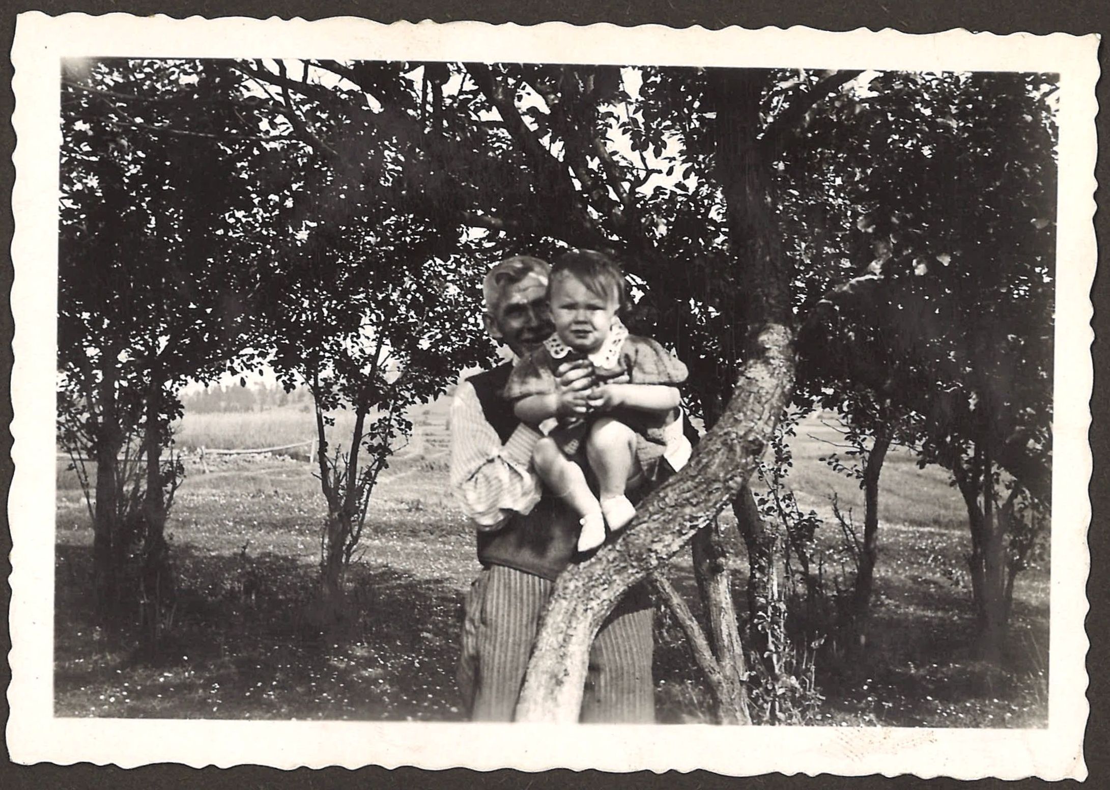 Jolantka Rodak ze starszym mężczyzną w sadzie z kwiatkami przy polnej drodze (oszac. 1938)